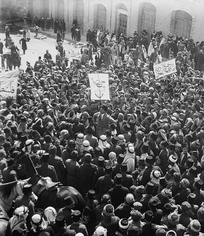 הפגנה של ערבים בשער שכם בירושלים ב-8 במרץ 1920. המלל בכרזות תומך בסיפוחה של ארץ ישראל, באותה העת רובה תחת משטר צבאי בריטי וחלקה הצפוני בשליטה צבאית צרפתית, לממלכה הערבית של סוריה שזה עתה קמה בראשותו של המלך פייסל. צילום: American Colony (Jerusalem). Photo Dept.