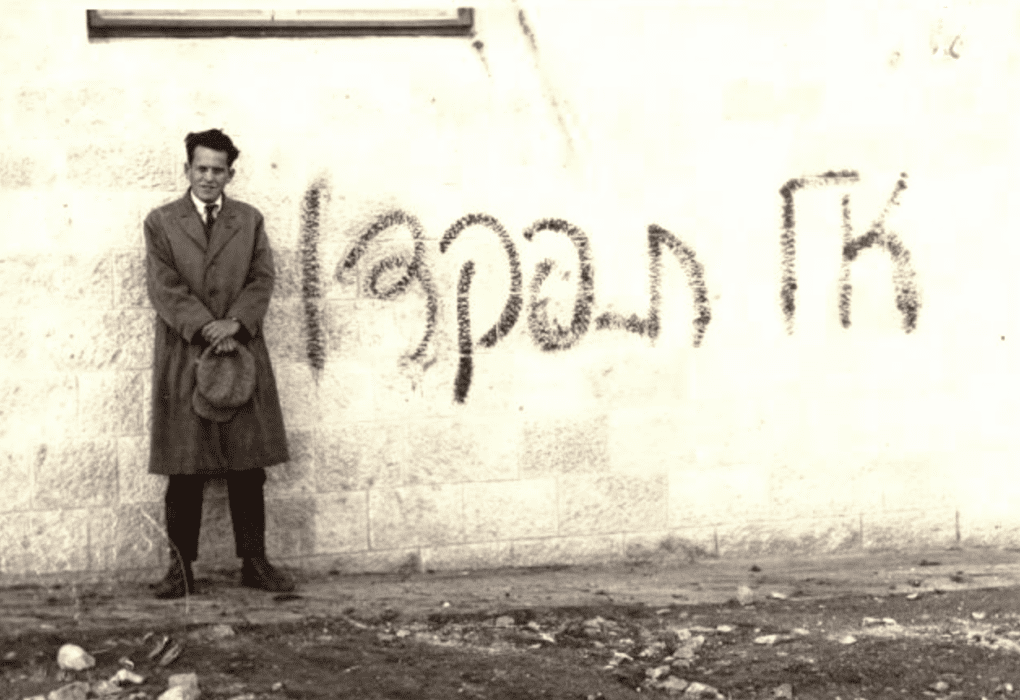 אב"א אחימאיר עומד ליד קיר ועליו גרפיטי: אל תִפּקדוּ", כנגד מפקד האוכלוסין הבריטי, 1931. צילום: לא ידוע.