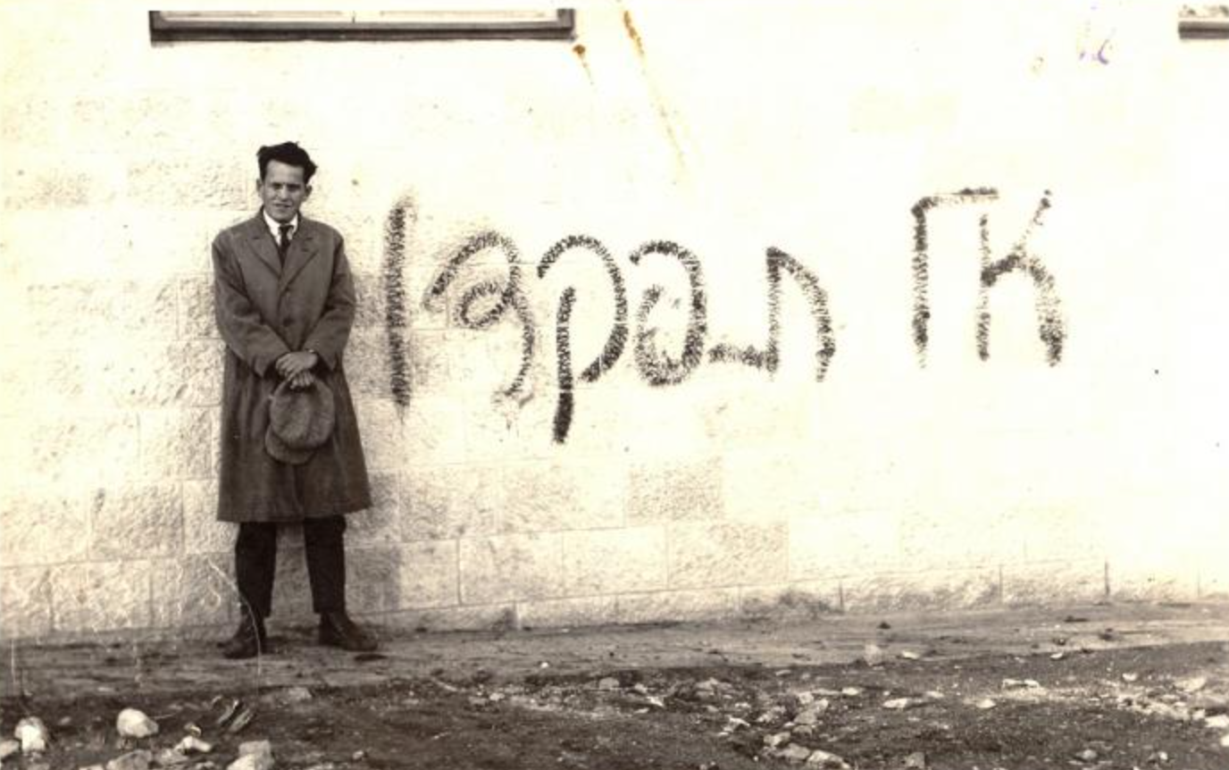 אב"א אחימאיר עומד ליד קיר ועליו גרפיטי: אל תִפּקדוּ", כנגד מפקד האוכלוסין הבריטי, 1931. צילום: לא ידוע.